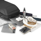 Eminence black leather waterproof backpack with multiple compartments and USB port, surrounded by laptop, camera, headphones, and travel essentials.