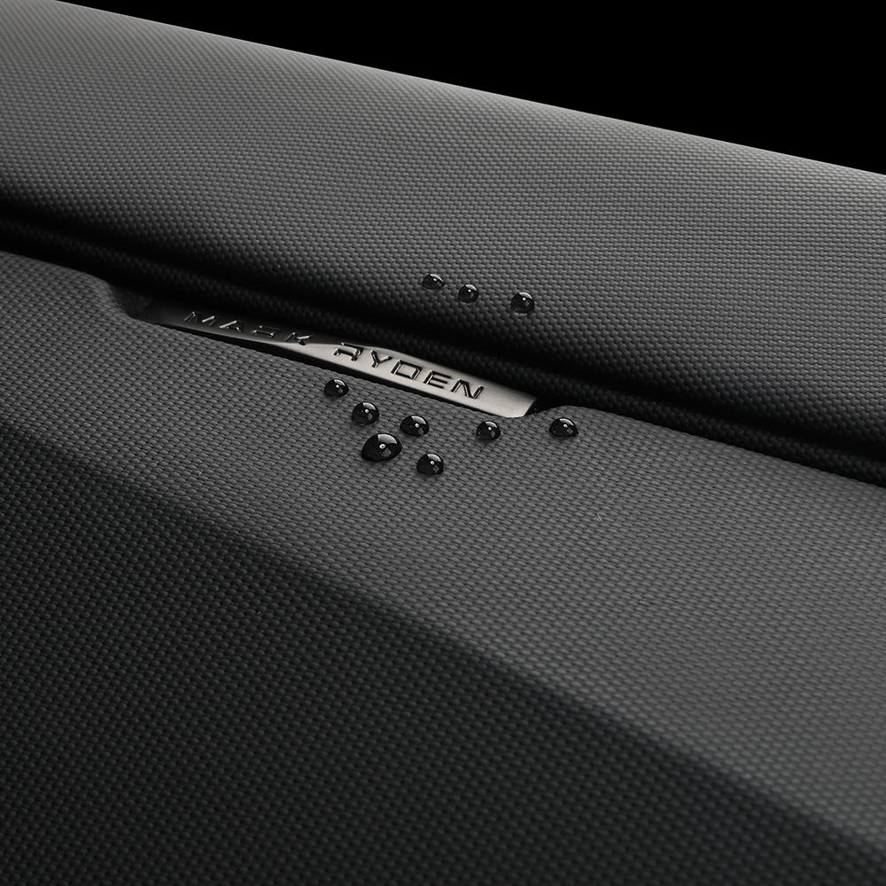 Black textured Mark Ryden Diamond Facets crossbody bag with water droplets demonstrating waterproof feature.