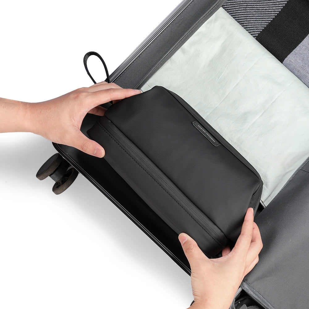 Black Switchstorage V toiletry bag with wet and dry compartments being placed into a suitcase for organized travel.