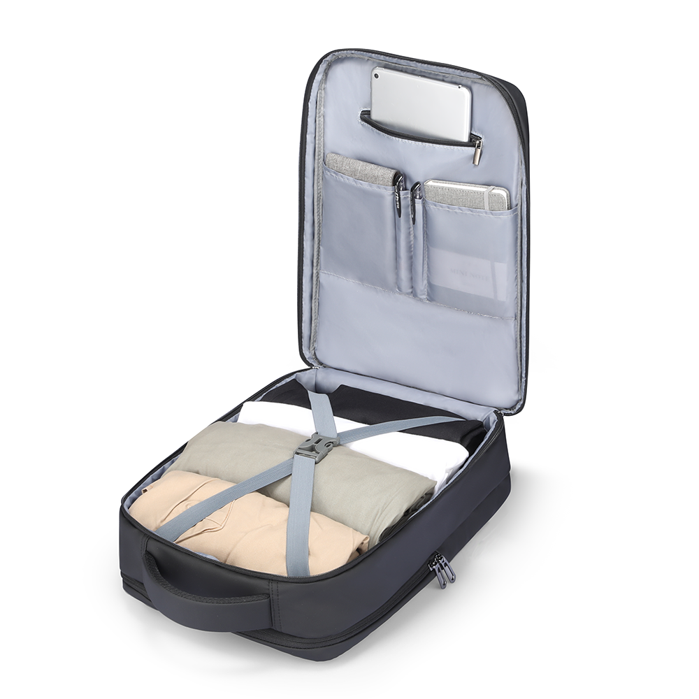 Black business multi-layer 15.6 inch laptop backpack with gray interior, open to show compartments holding folded beige, gray, and white clothes secured by straps, plus a tablet in the top pocket.