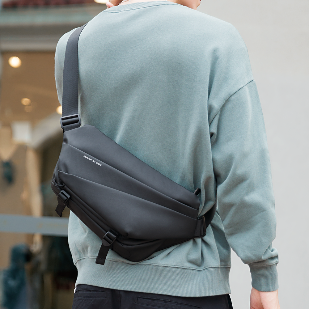 Mark Ryden Voyager dark gray leather messenger bag with umbrella pocket, worn crossbody by a person in a light blue sweatshirt.