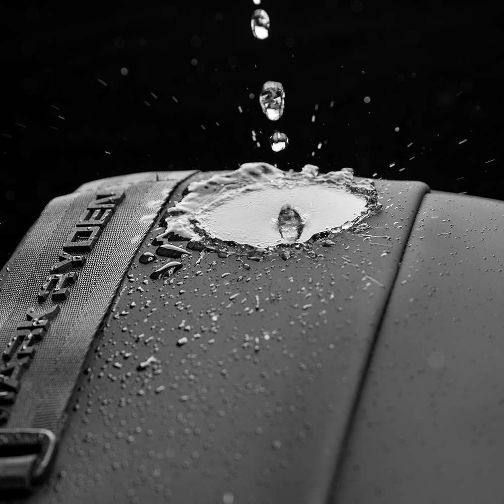 Black large capacity waterproof crossbody bag with water droplets splashing on surface, featuring Mark Ryden's commuter bag waterproof design.