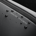 Close-up of MarkRyden Colonne high-capacity urban commuting crossbody bag with water-resistant textured fabric, embossed brand logo, and water droplets beading on surface.