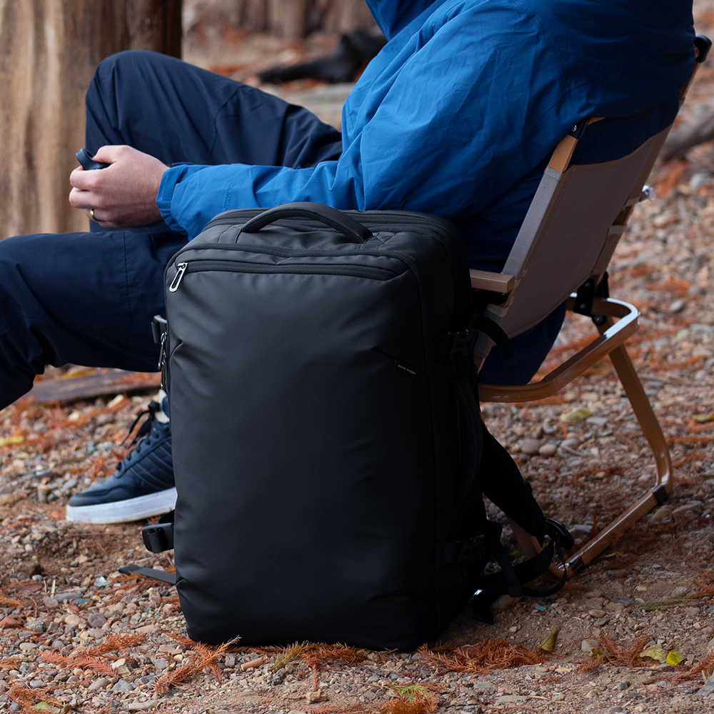 Person in blue jacket sits outdoors with MarkRyden black explorer multi-functional backpack